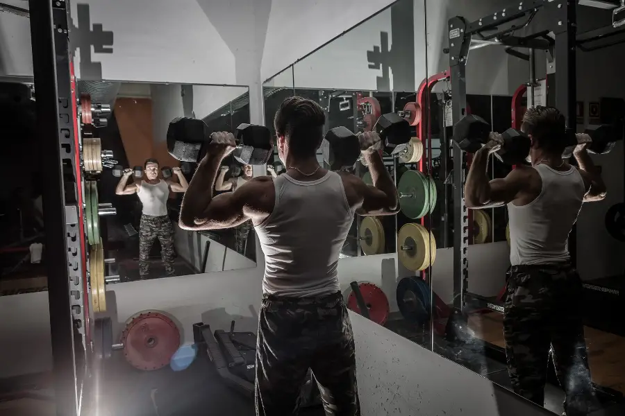 Man weightlifting in front of a mirror in a small home gym. 