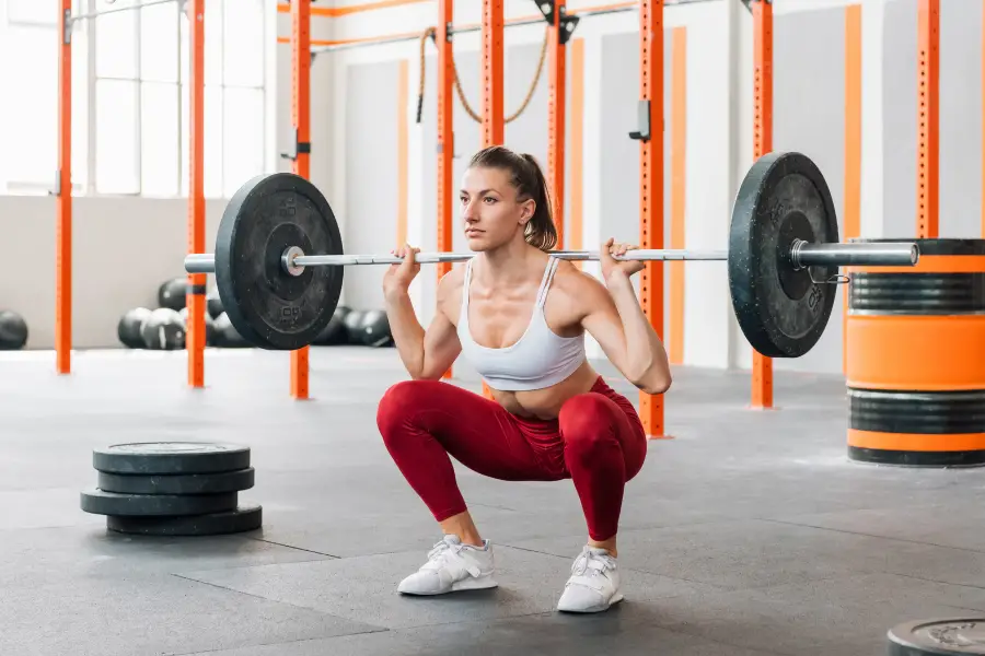 A woman barbell back squatting in a large gym.