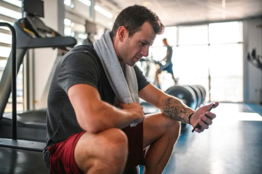 Image of a man using a phone in the gym while sitting on a treadmill.