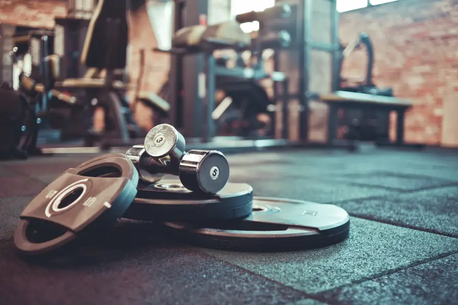 An image of weight plates and dumbbells laying on a rubber tile gym floor.