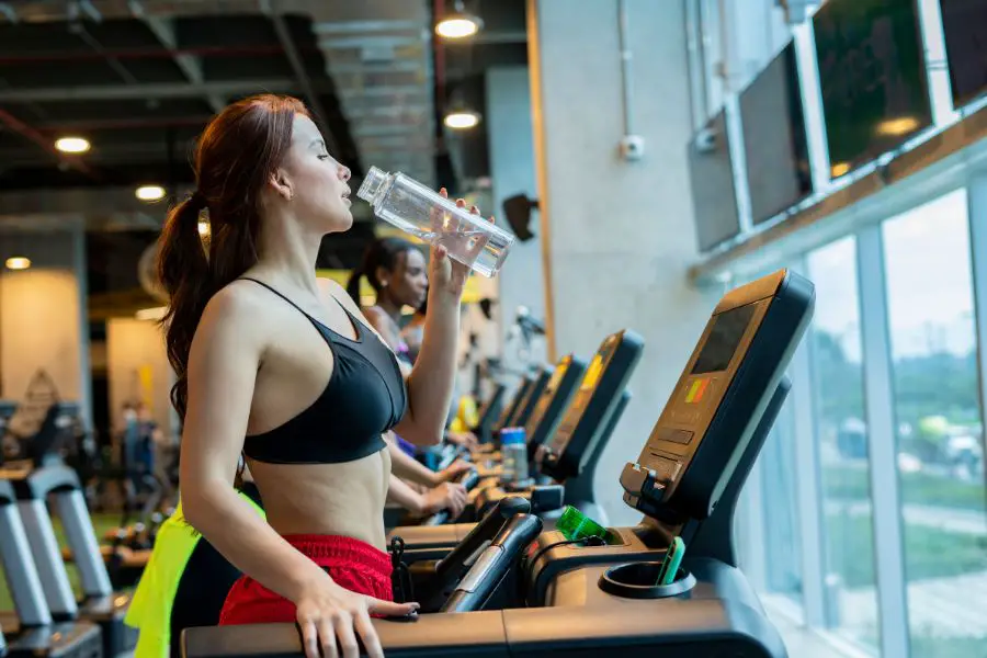 Image of a woman drinking water on a treadmill. 