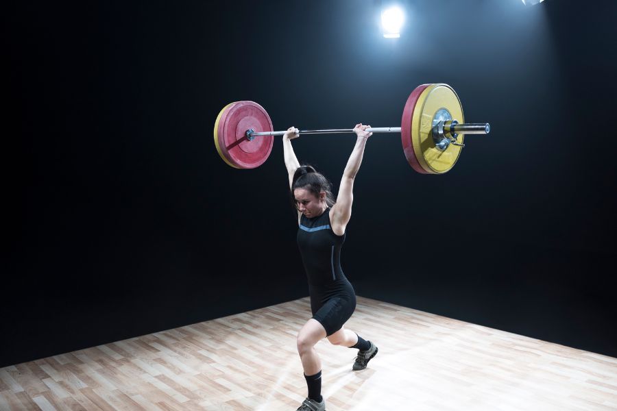 Image of a woman holding a barbell with bumper plates above her head.