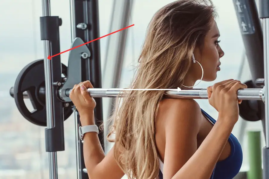 An image of a woman squatting in the smith machine with a red arrow pointing towards the guide rod. 